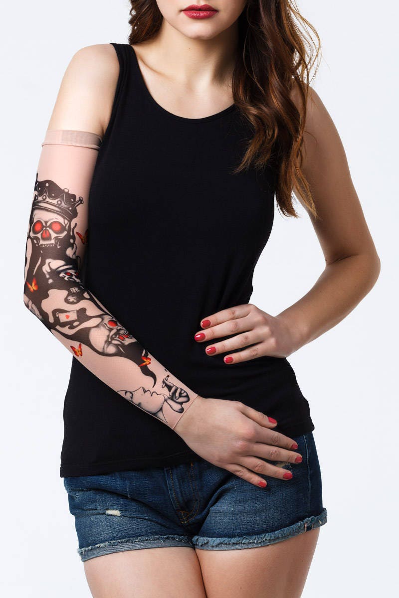 Rękaw z tatuażem czarnych czaszek z czerwonymi oczodołami, papierosów i kart do gry – na damskiej ręce, widok z przodu