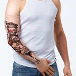 Rękaw z tatuażem czarnych czaszek z czerwonymi oczodołami, papierosów i kart do gry – na męskiej ręce, widok z przodu